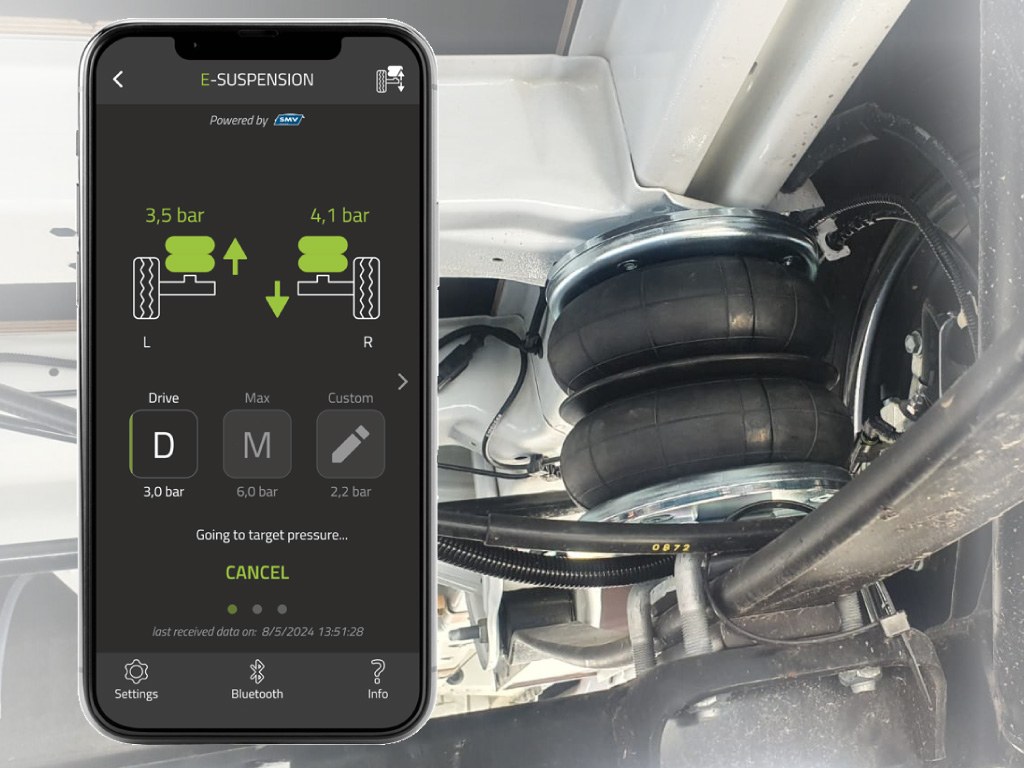 Smartphone mit der E-Suspension-App vor einem eingebauten Luftbalg an der Hinterachse